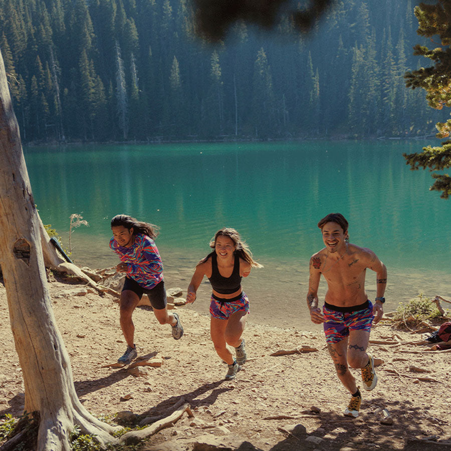 three hikers running alongside a lake